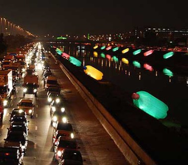 Imagem noturna de vinte garrafas infláveis pets gigantes iluminadas que foram instaladas em 2008 nas margens do rio Tietê