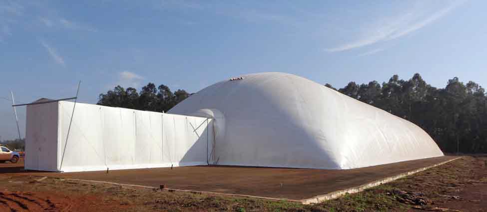 Tenda tipo cobertura pneumática temporária utilizada como galpão inflável na cor branca instalada sobre pavimento de concreto utilizada para armazenagem de sacaria de açúcar.
